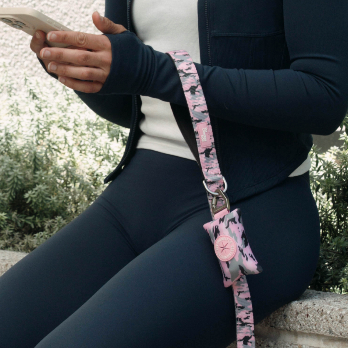 Pink camo poop bag holder attached to a hands-free dog leash worn around the wrist